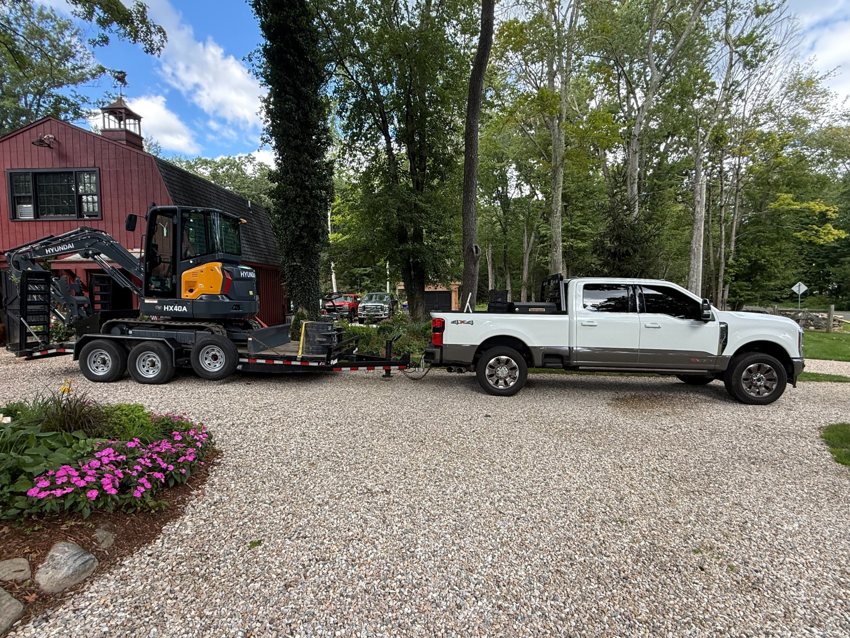 Truck, trailer, and compact excavator on site.